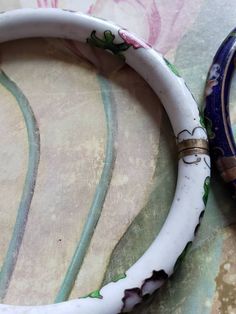 This is a vintage cloisonne bracelet. I have 2 for sale. One is dark blue with gold tone metal trim. This piece has a hinge and pulls open. There are some specks and flaws on the piece, as you can see in the images. The price reflects this. The bracelet measures a hair under 2.5 inches across on the interior. The other is white floral with gold trim. This piece has a hinge and pulls open. There is a chip in the bracelet as you can see in the images as well as specks on the piece. The price refle Vintage White Bangle Bracelets, Vintage Handmade Enamel Bangle, Vintage White Handmade Bangle, Handmade Vintage Enamel Bangle, Adjustable White Vintage Bangle, Vintage Round Enamel Bangle, Vintage Round Enamel Bracelets, Vintage Enamel Round Bracelets, Cloisonne Bracelet