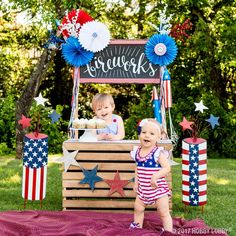 two babies are standing in front of an ice cream stand with red, white and blue decorations