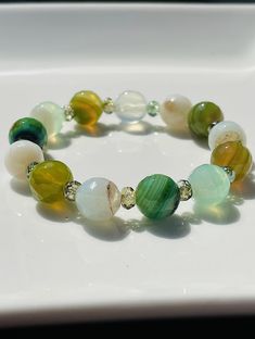 "Fun, multi-faceted 10mm agate gemstones with rich & soft greens, lemony green, cream/clear/white & olive create a lively \"grab & go\" stretch bracelet. Refresh yourself with an easy to wear piece that reminds you of the ever-popular Margarita cocktail! Agates are made up of chalcedony/quartz & are primarily formed within volcanic and metamorphic rocks. It is a stone for rebalancing the body, mind and spirit. Uniquely colorful, each agate has slight color variations & patterns that range from t Green Agate Stretch Bracelet With Natural Stones, Green Agate Crystal Bracelet With Gemstone Beads, Green Stretch Bracelet With Natural Stones, Green Faceted Round Bead Bracelets, Green Faceted Bracelets, Green Agate Hand-strung Bracelets, Green Agate Hand-strung Crystal Bracelet, Green Agate Bracelets With Natural Stones, Hand-strung Green Agate Stretch Bracelet