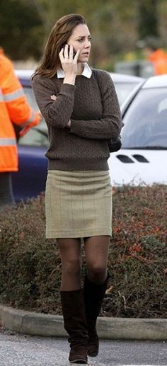 a woman walking down the street talking on her cell phone while wearing a skirt and knee high boots