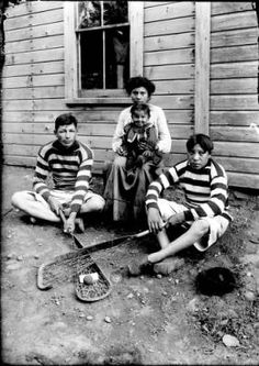 an old black and white photo of four people sitting on the ground in front of a house