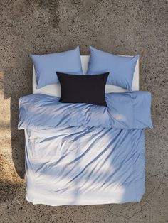 a bed with blue sheets and pillows on the floor next to a tree trunk, top view from above