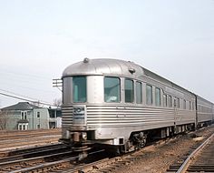 a silver passenger train traveling down tracks next to some houses and power lines in the background