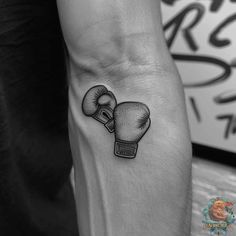 a black and white tattoo of two boxing gloves on the left arm, with one hand holding