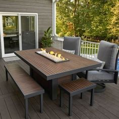 an outdoor table and chairs on a deck with fire pit in the center surrounded by trees