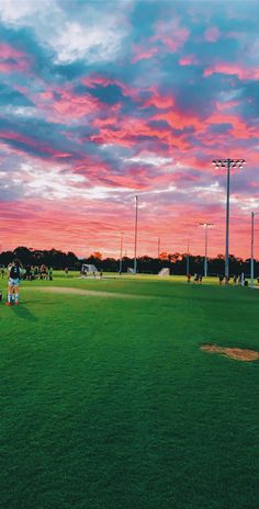 people are playing baseball on the field at sunset or dawn with pink and blue clouds