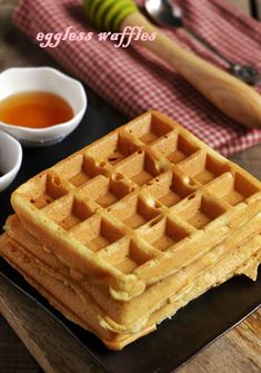 a waffle sitting on top of a black plate next to two cups of tea