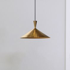 a gold colored pendant light hanging from a white wall next to a black table and chair