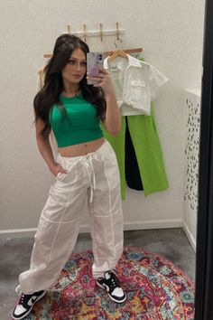 Mirror selfie featuring a fashion-forward outfit consisting of white cargo pants and a green tank top. The person is standing in front of a mirror, posing confidently while showcasing the trendy ensemble. The white cargo pants are loose-fitting with multiple pockets, paired with a green tank top that has a relaxed fit. The outfit exudes effortless chic, perfect for a casual day out or a springtime fashion statement. Sporty Summer Cargo Pants With Pockets, Sporty Summer Cargo Pants With Cargo Pockets, Casual Summer Cargo Parachute Pants, Sporty Wide-leg Cargo Pants For Spring, Versatile Parachute Pants With Pockets For Summer, Versatile Summer Parachute Pants With Pockets, Casual Summer Cargo Pants With Drawstring, Sporty Wide Leg Cargo Pants For Spring, Casual Parachute Pants With Cargo Pockets For Summer