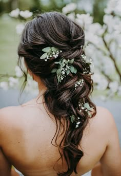 the back of a woman's head with flowers in it and greenery on her hair