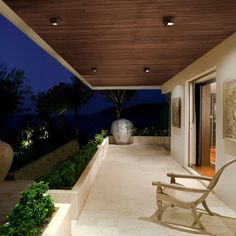 an outdoor area with chairs and plants at night time, along with lights on the ceiling