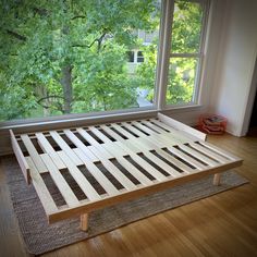 a wooden bed frame sitting on top of a hard wood floor next to a window