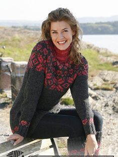 a woman sitting on top of a wooden bench next to a body of water and grass