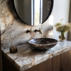 a bathroom sink sitting under a round mirror next to a vase with flowers in it