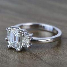 an emerald cut diamond ring sitting on top of a wooden table