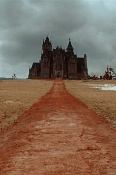 a dirt road in front of a large building on top of a dry grass field