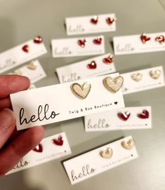 a person is holding up some small heart shaped studs in front of cards with name tags attached to them