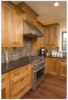 a kitchen with wooden cabinets and black counter tops, stainless steel appliances and wood flooring