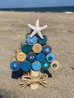 a small tree made out of wine corks on the beach with a starfish