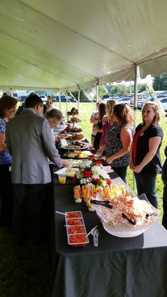 several people are standing at a buffet table with food on it and one person is holding a knife