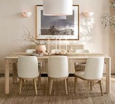 a dining room table with white chairs and an art piece on the wall above it