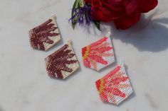 three pieces of beaded art sitting next to a red flower on a white table