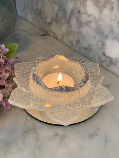 a candle that is sitting on a table next to some flowers and a glass bowl