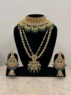 Full bridal set in hues of green for the beautiful bride! This glamorous bridal kundan necklace set features shimmering faux kundan stones intricately handcrafted in meenakari and decorated with green beads. The set comprises of 9 pcs including a long necklace, a princess necklace, pair of beautiful earrings with kaan chains, a mathapatti, a nose rings bajubandh and a pair of haathphool. Dimensions: Long Necklace Length-16 Inches Princess Necklace Width-3.75 Inches Earrings Length-4.75 Inches Earrings Width-2.75 Inches Kaanchain Length-5.25 Inches Weight of Each Earring-68 gms Matha Patti Tika Drop-5.25 Inches Nosering Dia-1.75 Inches All products are manufactured using traditional skills from our rich heritage of crafts.  The process of these crafts is essentially manual. Hence, any irreg Wedding Green Meenakari Anarkali Set, Green Meenakari Anarkali Set For Wedding, Green Wedding Anarkali Set With Meenakari, Green Kundan Temple Jewelry Set, Green Kundan Sets With Tilla, Green Kundan Bridal Necklace Hand Set, Green Kundan Necklace With Cutdana For Wedding, Heavy Green Bridal Sets For Wedding, Green Kundan Necklace For Wedding And Festivals