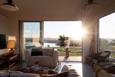 a man walking into a living room with sliding glass doors that lead out to a lake