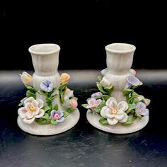 two white vases sitting on top of a black table with flowers painted on them