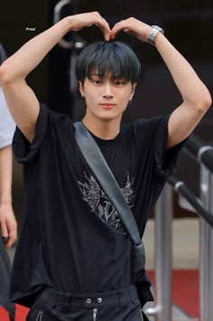 a young man making a heart shape with his hands while standing in front of stairs