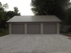 two garages are shown in front of some trees and gravel on the side of a road