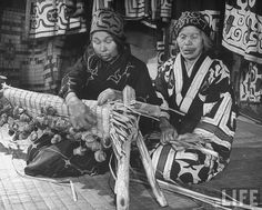 two people sitting on the ground with sticks in their hands and one person holding something