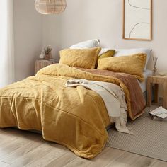 a bed with yellow comforter and pillows in a white room next to a window