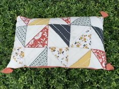 a patchwork pillow sitting on top of a lush green field