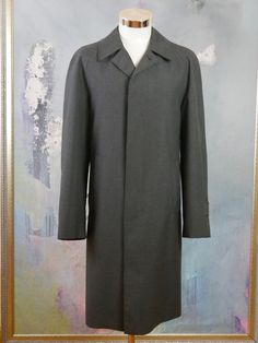 This charcoal gray overcoat is crafted from a high-quality wool-blend fabric, has a notch collar, and closes in the front with three concealed black buttons. The raglan style long sleeves feature a buttoned cuff strap, and the coat has two slanted storm pockets. The coat is lined in a black satin polyamid fabric (with one inner pocket), and a center vent in the back ensures complete ease of movement. Brand label: Oratop (Finland) Size: 44 US/UK Material: 45% Wool, 55% Polyester Condition: Near M Gray Long Wool Coat For Business, Gray Long Sleeve Wool Coat For Formal Occasions, Fitted Gray Outerwear With Hidden Button Closure, Gray Business Outerwear With Suit Collar, Gray Wool Outerwear With Concealed Placket, Tailored Gray Wool Coat, Gray Notch Lapel Wool Coat For Business, Gray Wool Notch Lapel Coat For Business, Gray Outerwear With Concealed Placket For Work