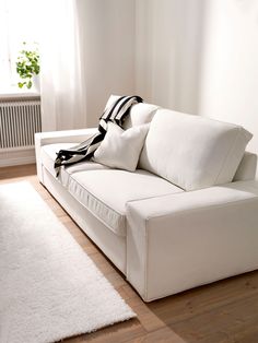 a white couch sitting on top of a hard wood floor next to a window in a living room