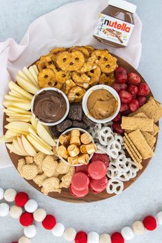 a platter filled with cookies, pretzels, fruit and nuts next to a box of nutella