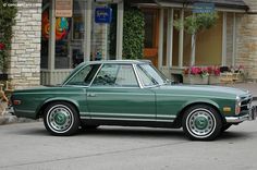 a green car parked in front of a building on the side of the road next to a dog