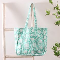 a green and white bag sitting on top of a wooden chair next to a plant