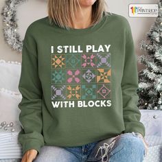 a woman wearing a green sweatshirt with the words i still play with blocks on it