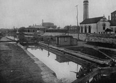 an old black and white photo of a canal in the middle of town with buildings on either side