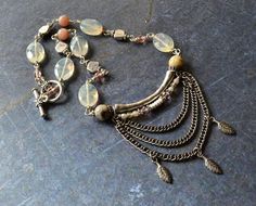 I love how soft and pretty this necklace is. Yellow quartz pairs beautifully with the faceted crazy lace agate and peach moonstone. Lots of silver accent beads and additional swarovski crystals adds a touch of sparkle. Layers of czech glass beads, leaf charms, and antique silver chains drape from a curved tube bead giving it lots of movement and interest. Finished off with a leaf patterned silver plated toggle clasp. Length: 10 3/4"All components and materials used in this design are listed in t Luxury Artisan Soldered Necklaces, Handmade Bohemian Apricot Jewelry, Handmade Apricot Bohemian Jewelry, Bohemian Apricot Jewelry For Gift, Boho Statement Necklace, Tube Necklace, Multi Chain Necklace, Modern Necklace, Yellow Quartz