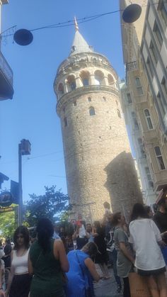 many people are walking around in front of a tall brick tower with a clock on it's side