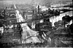 black and white photo of an industrial area with water in the background, looking down at buildings