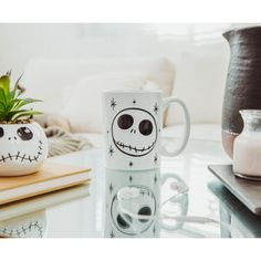 a white coffee mug sitting on top of a table next to a potted plant