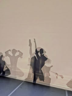 the shadow of two people dancing in front of a wall with their hands up and arms raised