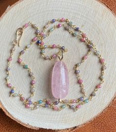 "This soft pastel colored multi Sapphire necklace featuring a stunning centerpiece, a large peachy pink Morganite pendant, captures the essence of the season, radiating femininity. The large, smooth polished natural pink Morganite pendant measures 2.2 x 1.1 cm. This alluring gemstone is suspended from a 19.5\" (50 cm) long multicolor Sapphire rosary chain, fastened by a hand forged 14k gold filled hook clasp. The sparkly multi Sapphire rosary chain boasts a luxurious 22k gold vermeil finish. The Pink Spiritual Crystal Necklaces, Pastel Gemstone Beads Jewelry For Gifts, Elegant Pink Faceted Crystal Necklace, Delicate Single Strand Pink Necklace, Delicate Pink Single Strand Necklace, Feminine Pink Pendant Jewelry, Bohemian Pink Jewelry With Gemstone Accents, Delicate Pink Teardrop Pendant Necklace, Bohemian Pink Crystal Pendant Necklace