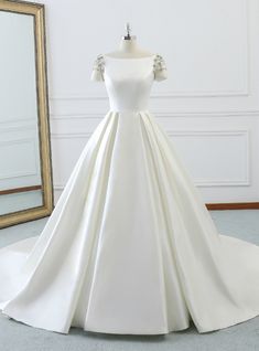 a white wedding dress on display in front of a mirror with a gold framed frame