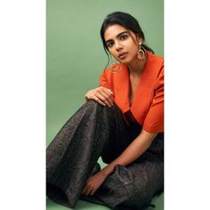 a woman sitting on the ground wearing an orange top and black pants with gold hoop earrings